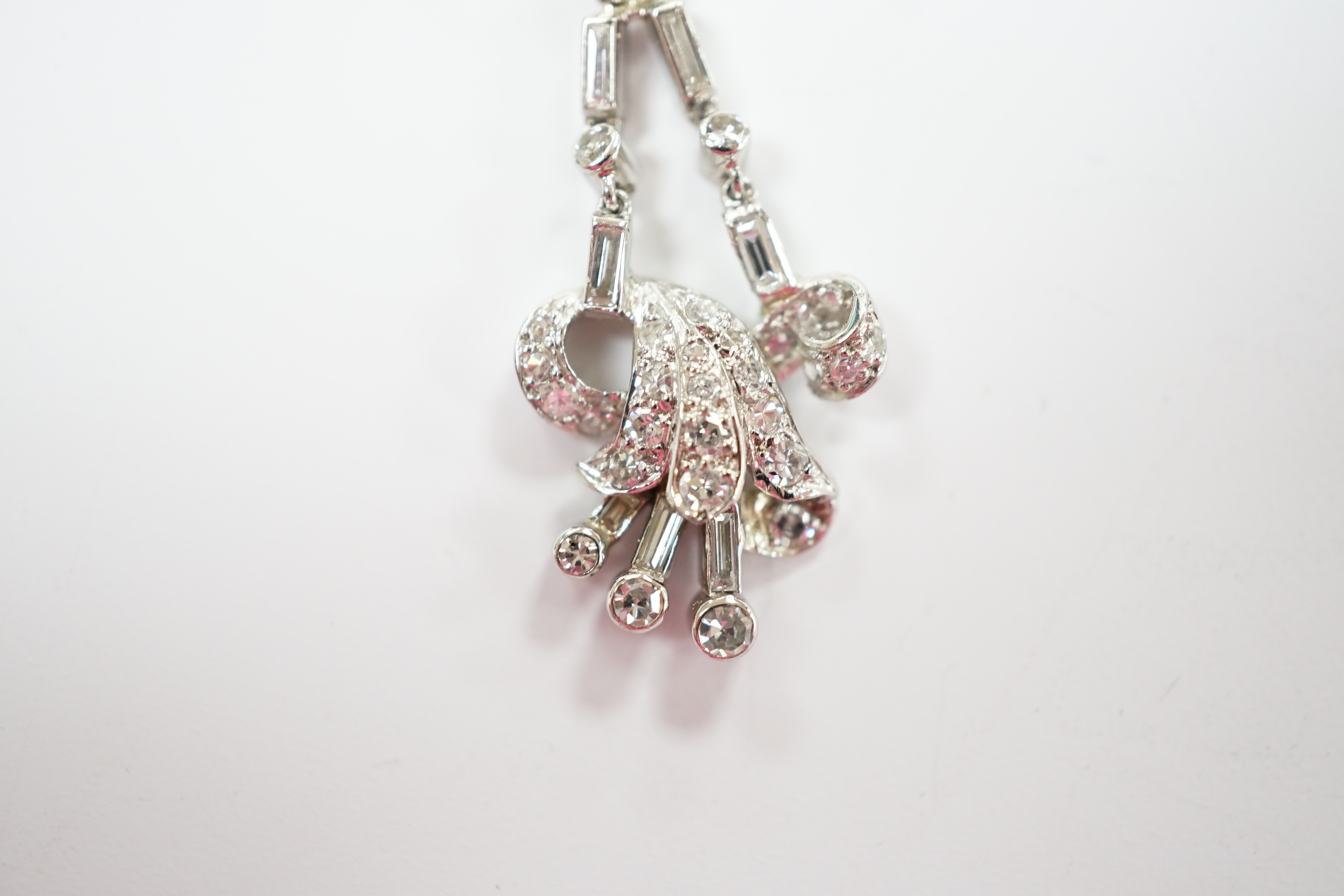 A white metal baguette and round cut diamond cluster set scroll pendant, overall 33mm, gross weight 3.6 grams.